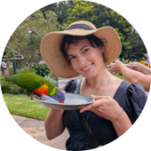 Woman wearing hat holds plate that parrot is eating from