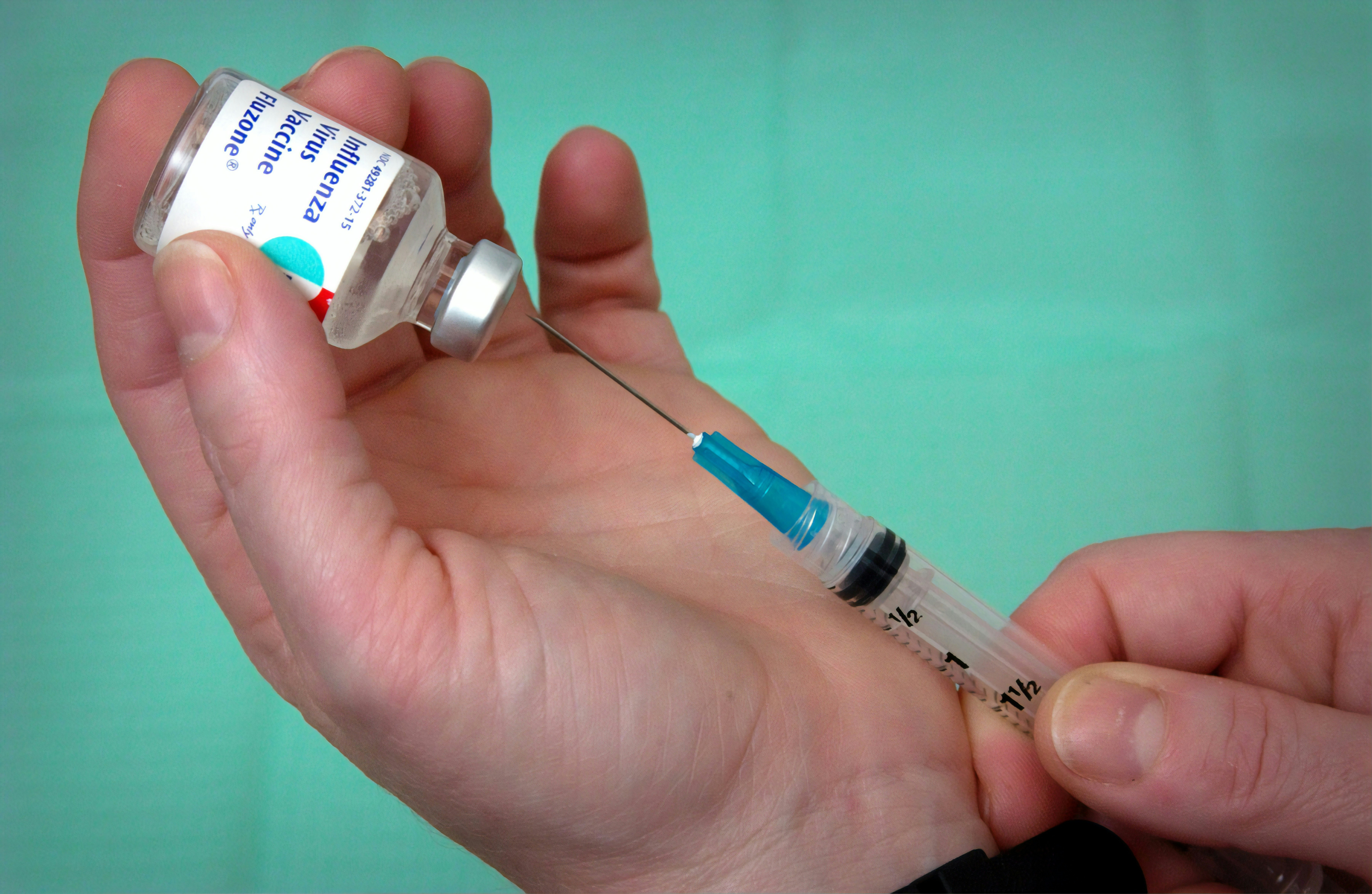 two hands use syringe to extract flu vaccine from glass vial