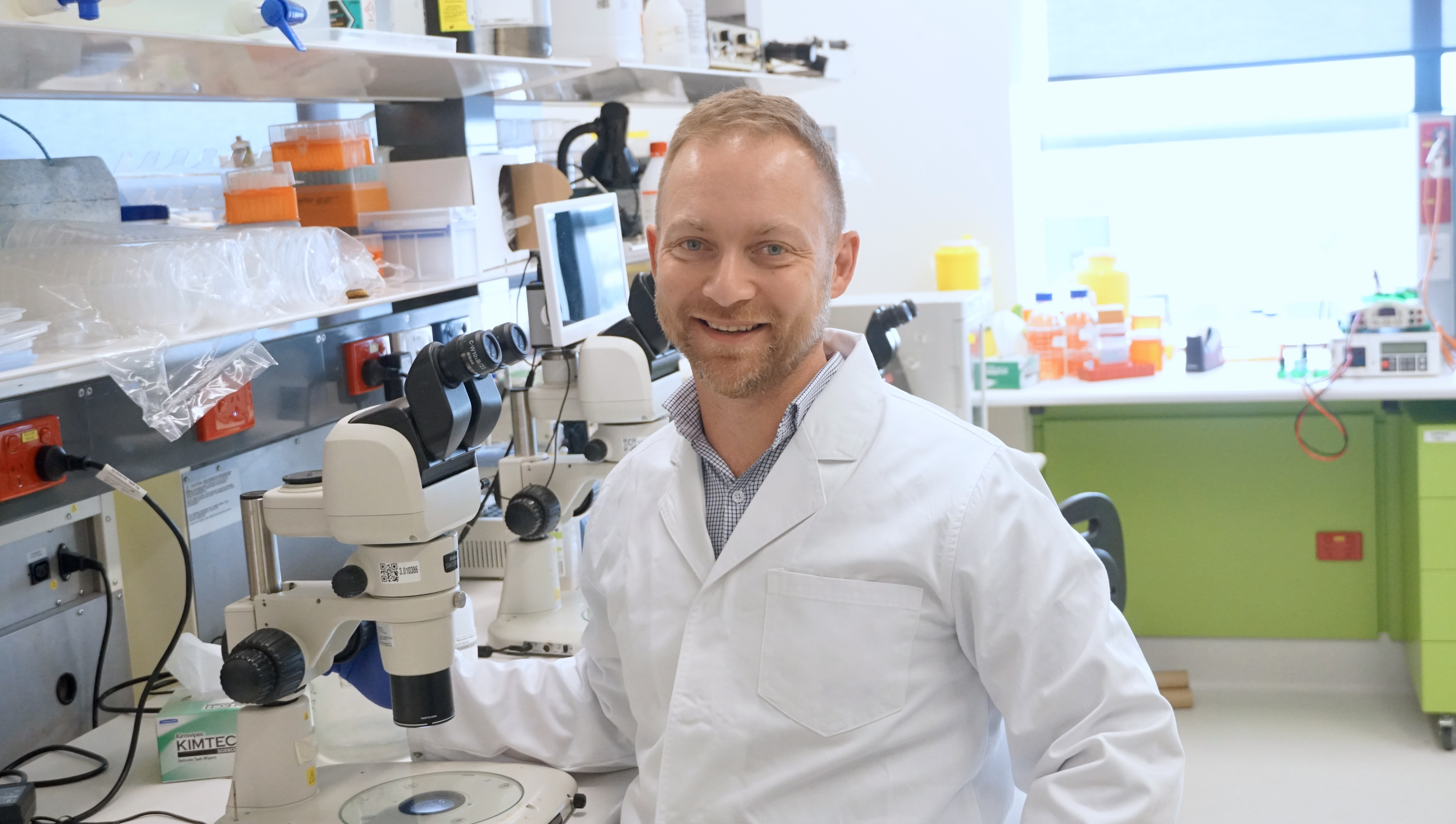 man in white lab coat at microscope 
